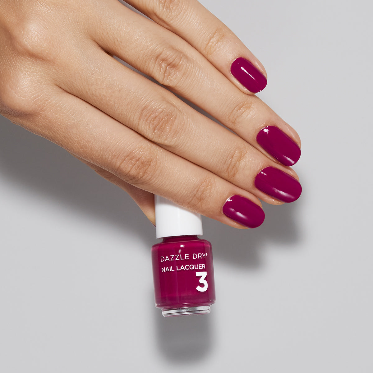 Hand with Raspberry Rush painted on nails holding mini lacquer botte
