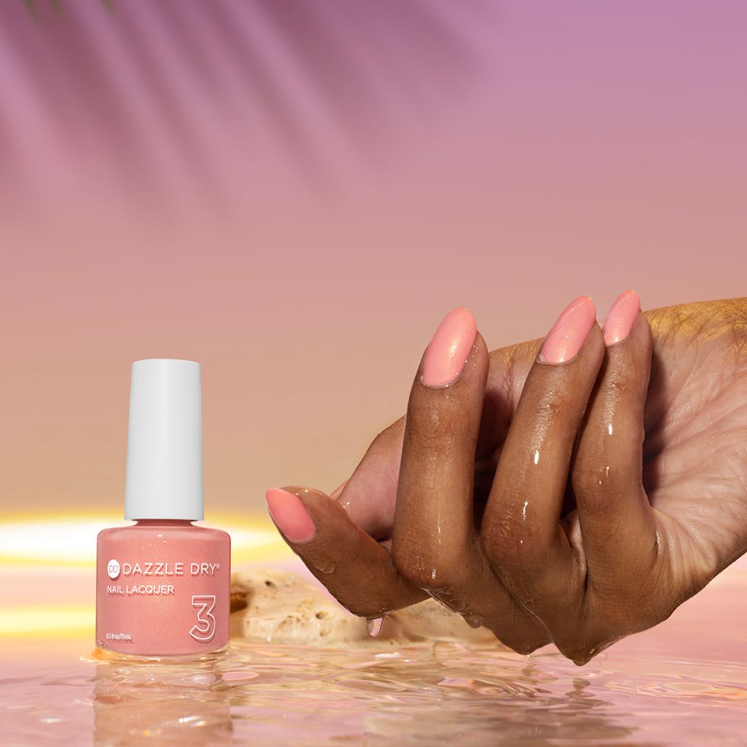 Hand with Sunset Glow painted on nails next to nail lacquer bottle