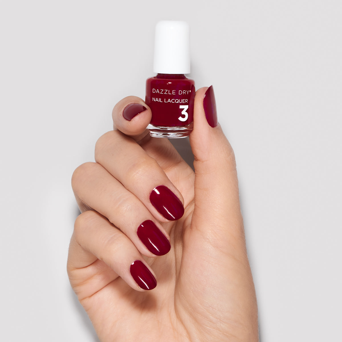 Hand with Fast Track Cherry painted on nails holding mini lacquer bottle