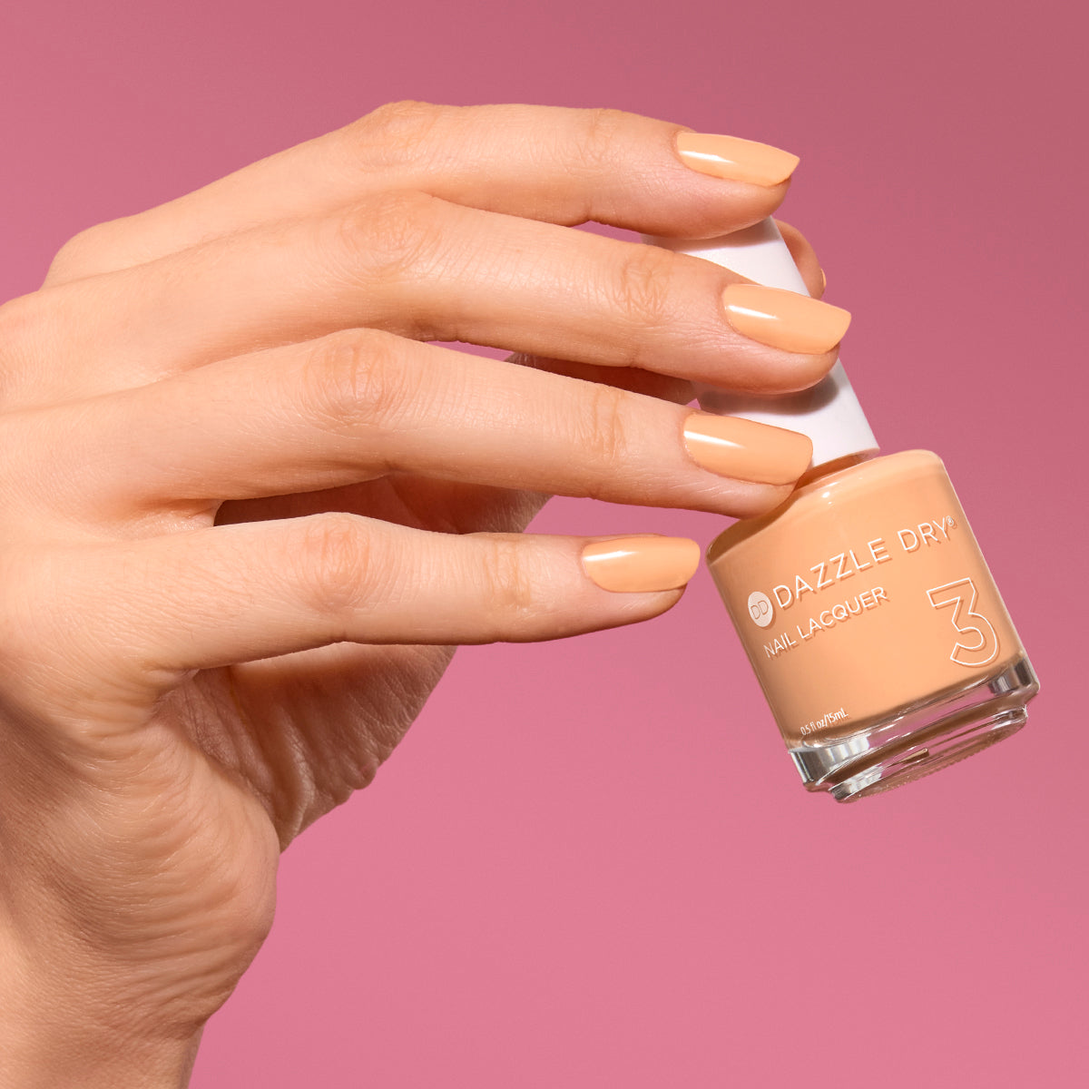Hand with Creamsicle Sorbet painted on nails holding full size lacquer bottle