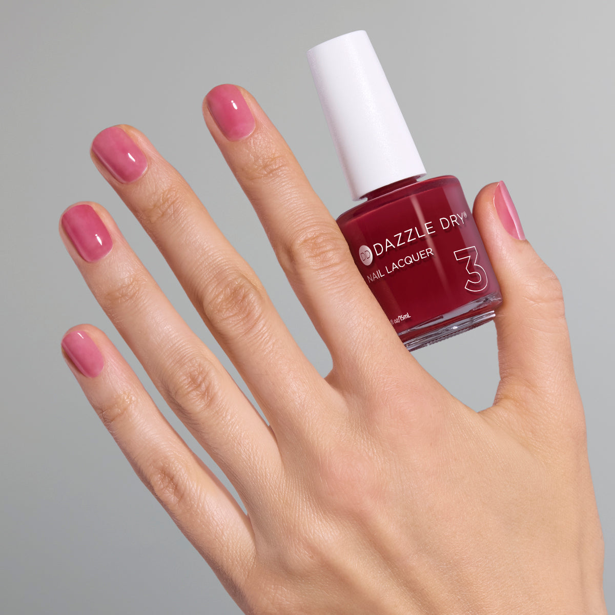 Hand with Ring Toss painted on nails holding full size lacquer bottle