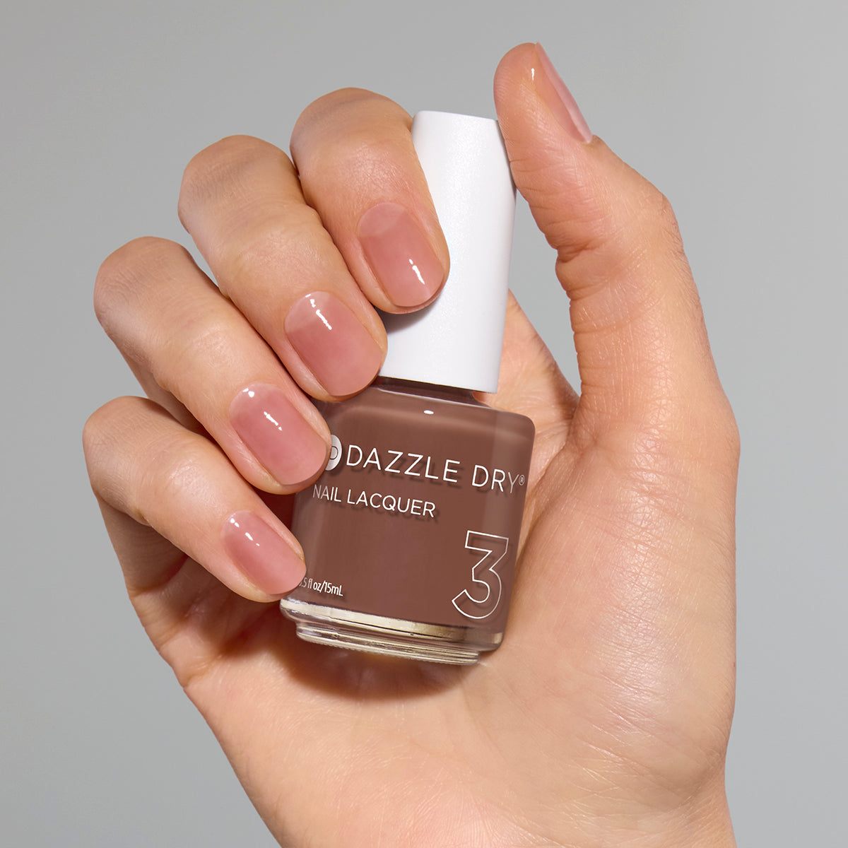 Hand with Toffee Crunch painted on nails holding full size lacquer bottle
