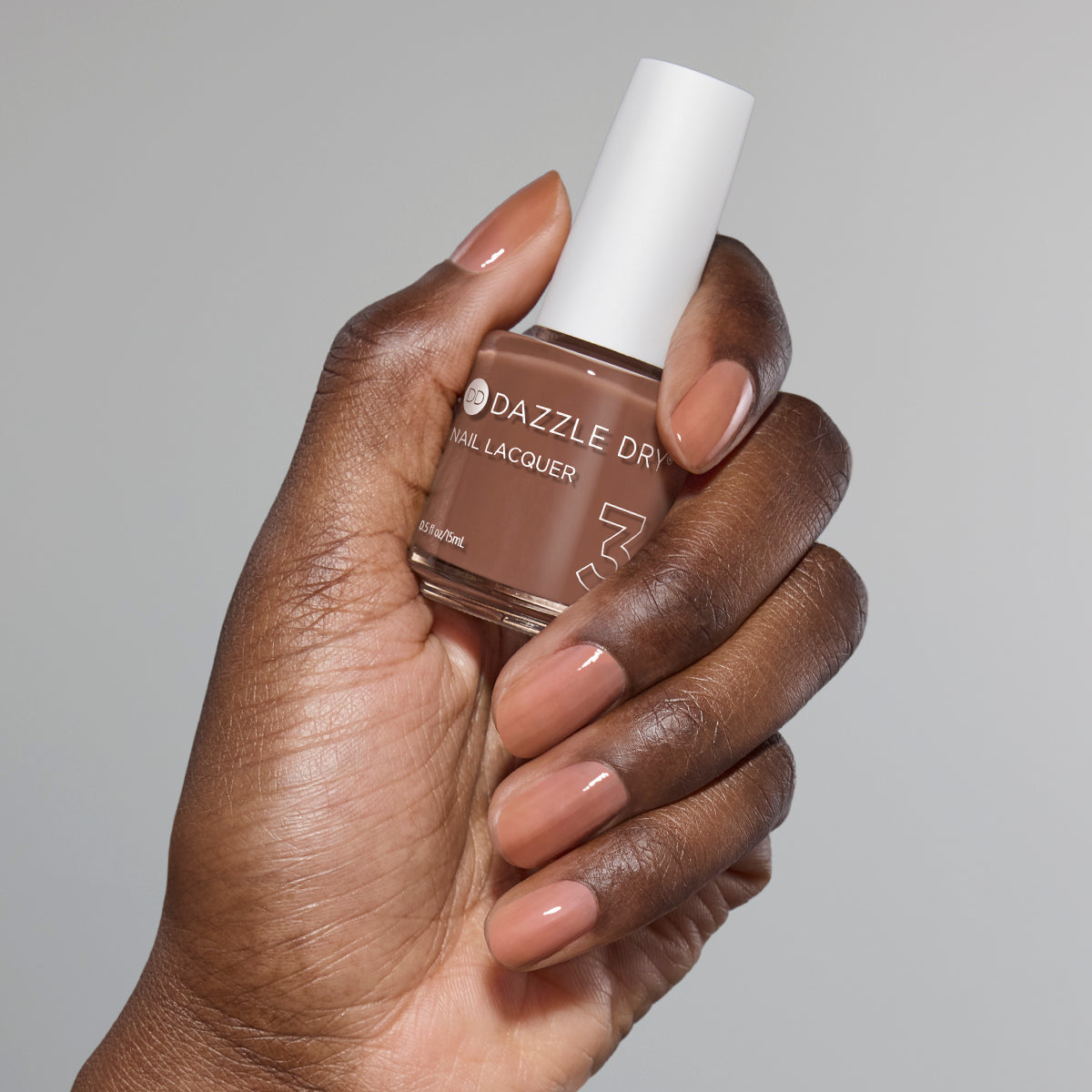 Hand with Toffee Crunch painted on nails holding full size lacquer bottle