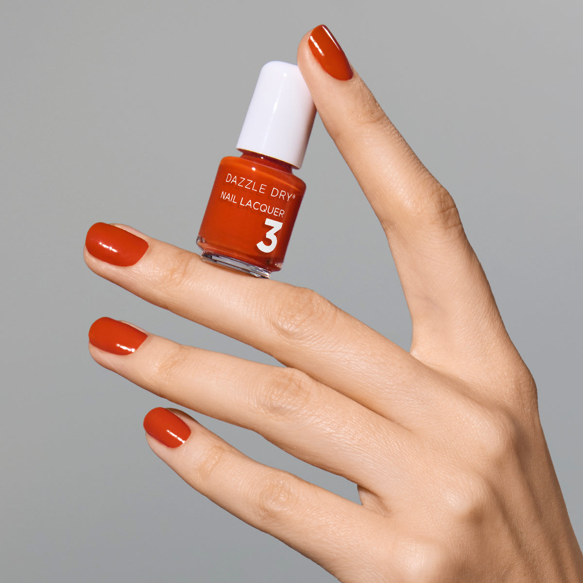 Hand with Orchard painted on nails holding mini lacquer bottle