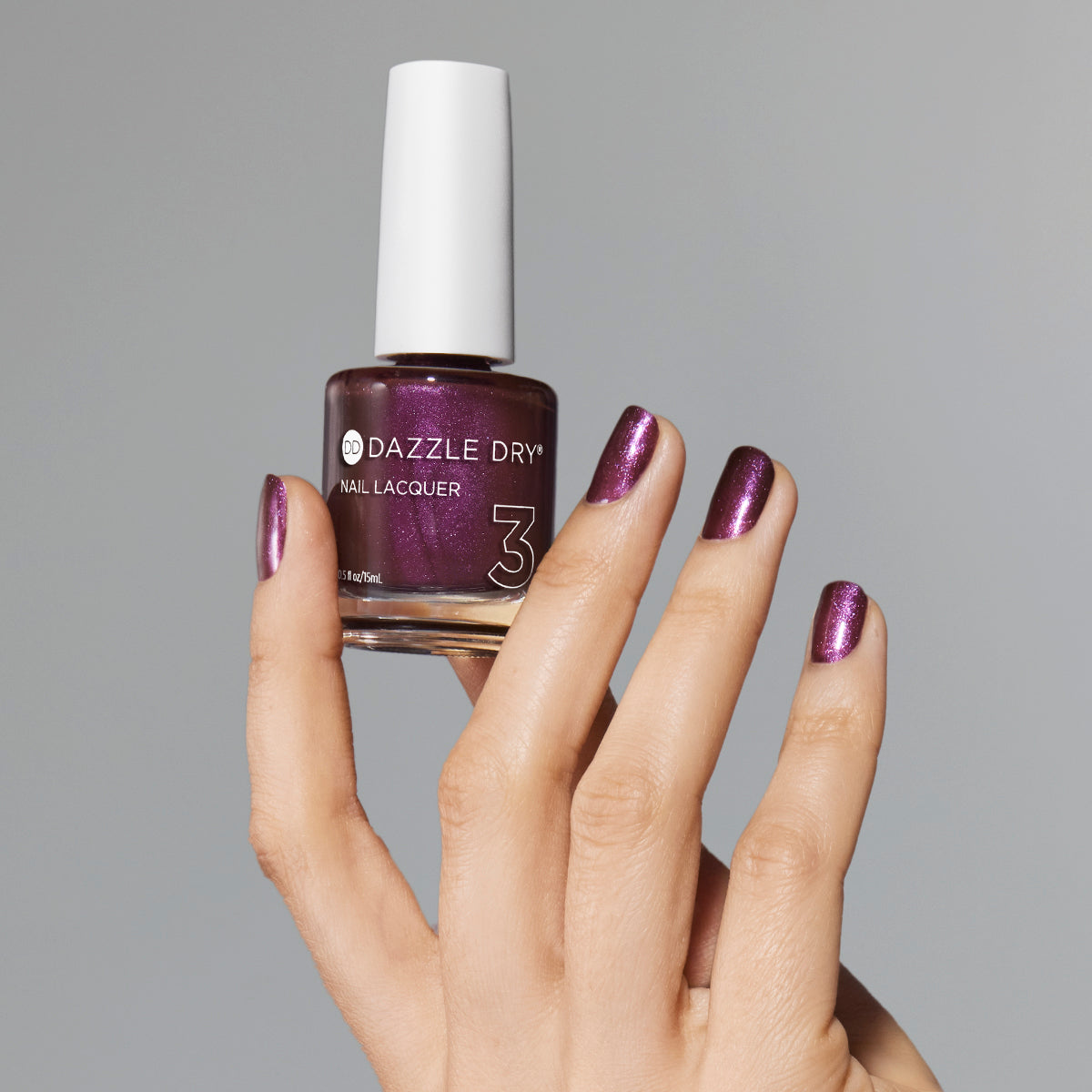 Hand with Spiced Plum painted on nails holding lacquer bottle