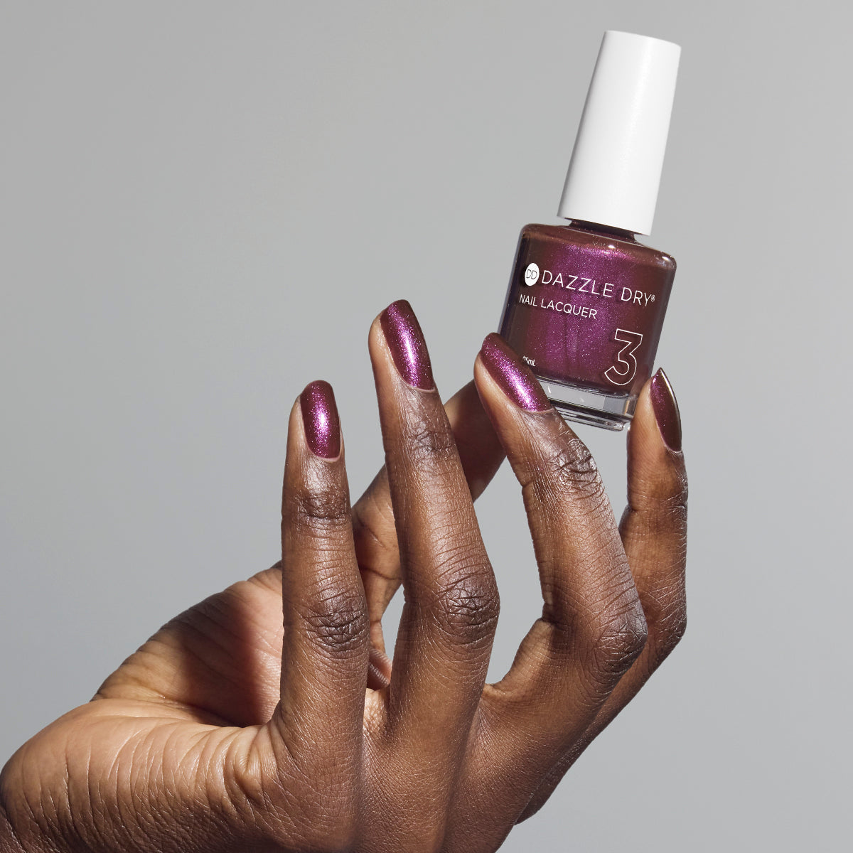 Hand with Spiced Plum painted on nails holding lacquer bottle