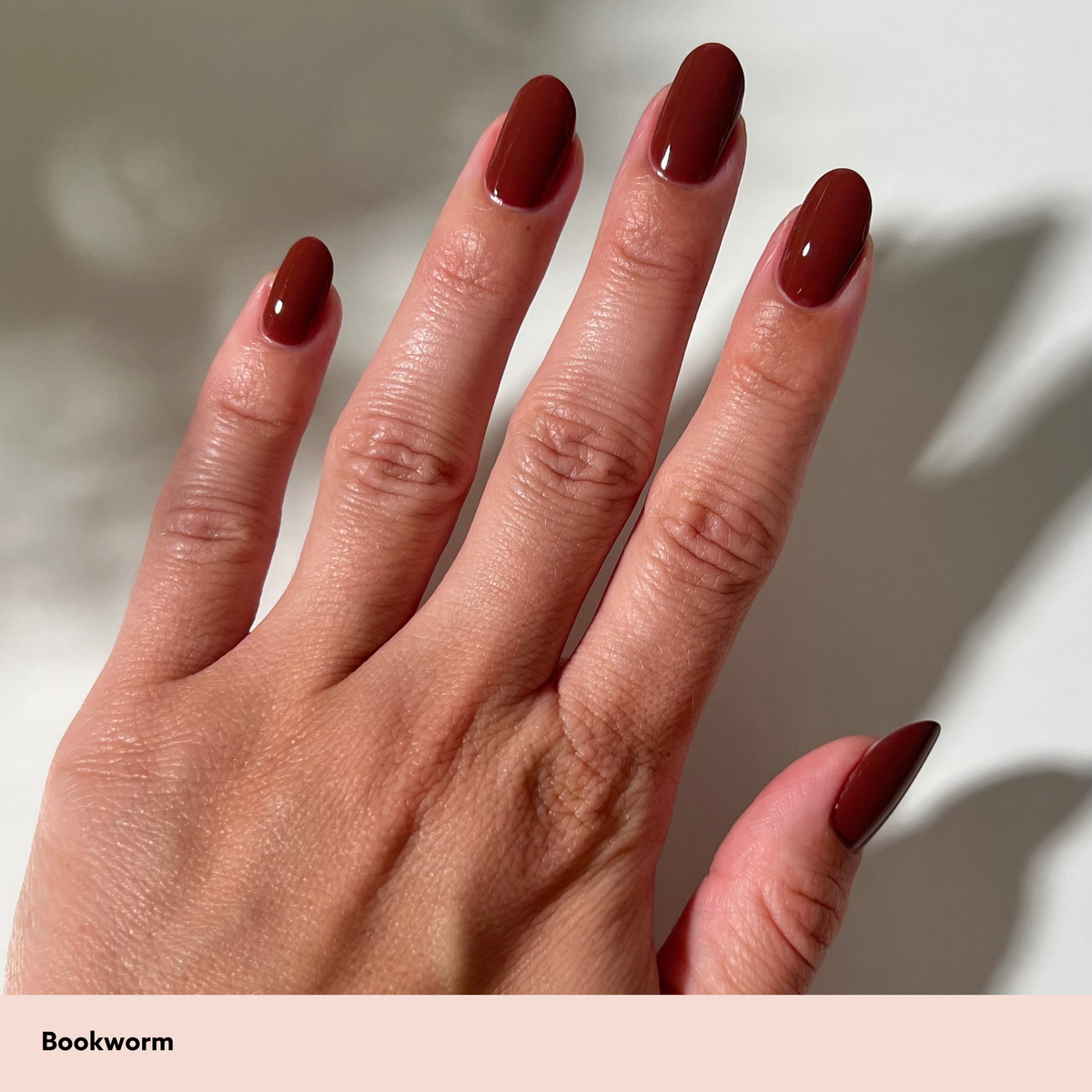 A close-up of a hand with long, almond-shaped nails painted in a deep, glossy dark red or oxblood shade. The text 'Bookworm' appears in a black font on a pale pink banner at the bottom left.