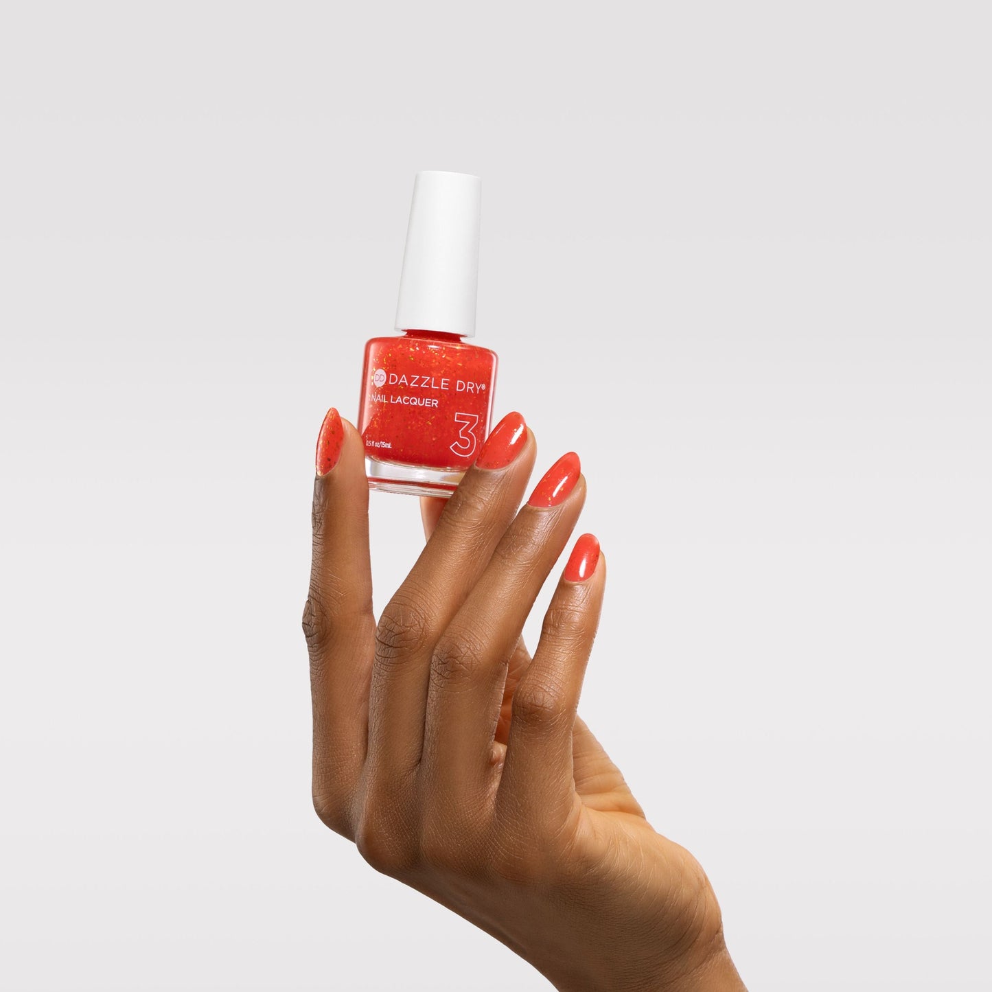 Hand holding a bottle of red nail polish with a white cap on a light gray background
