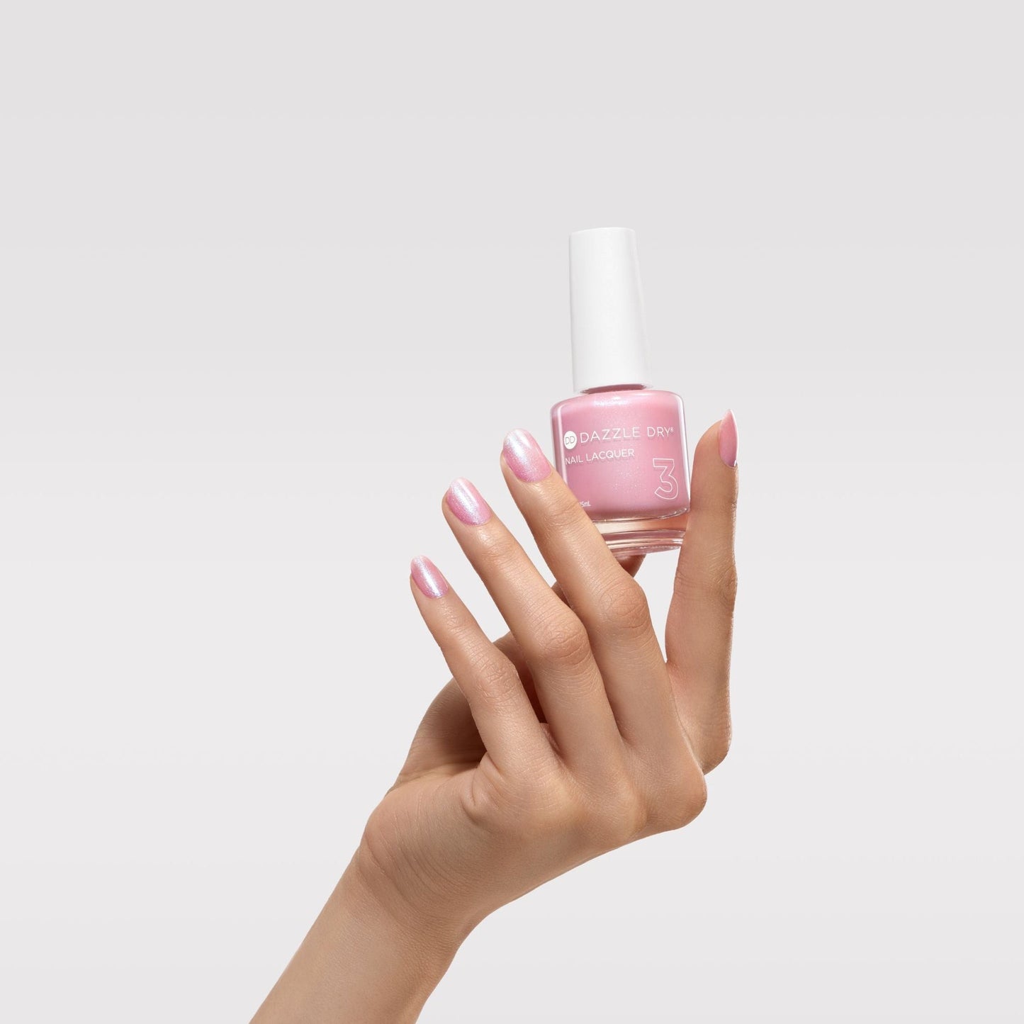 hand holding pink nail polish with nails painted