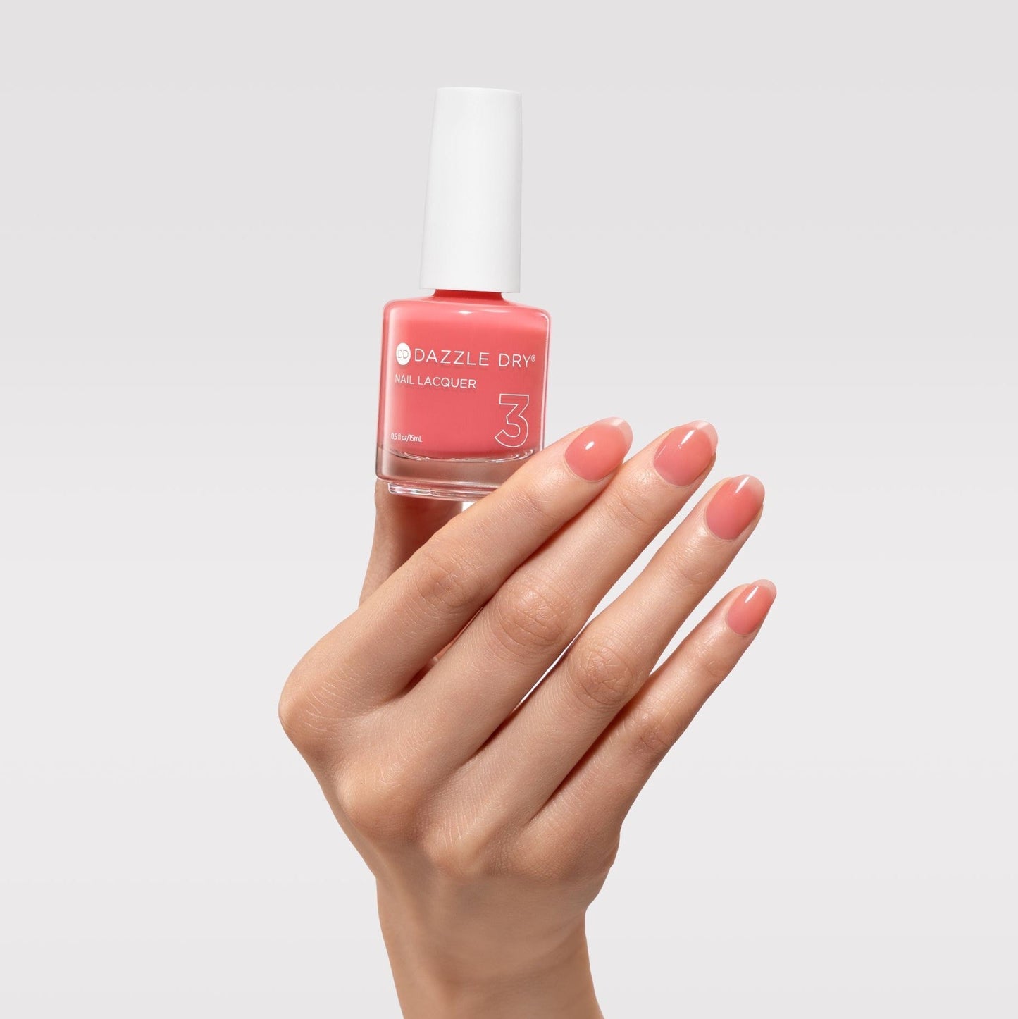 Hand holding a bottle of Dazzle Dry nail polish with matching pink nails on a light gray background