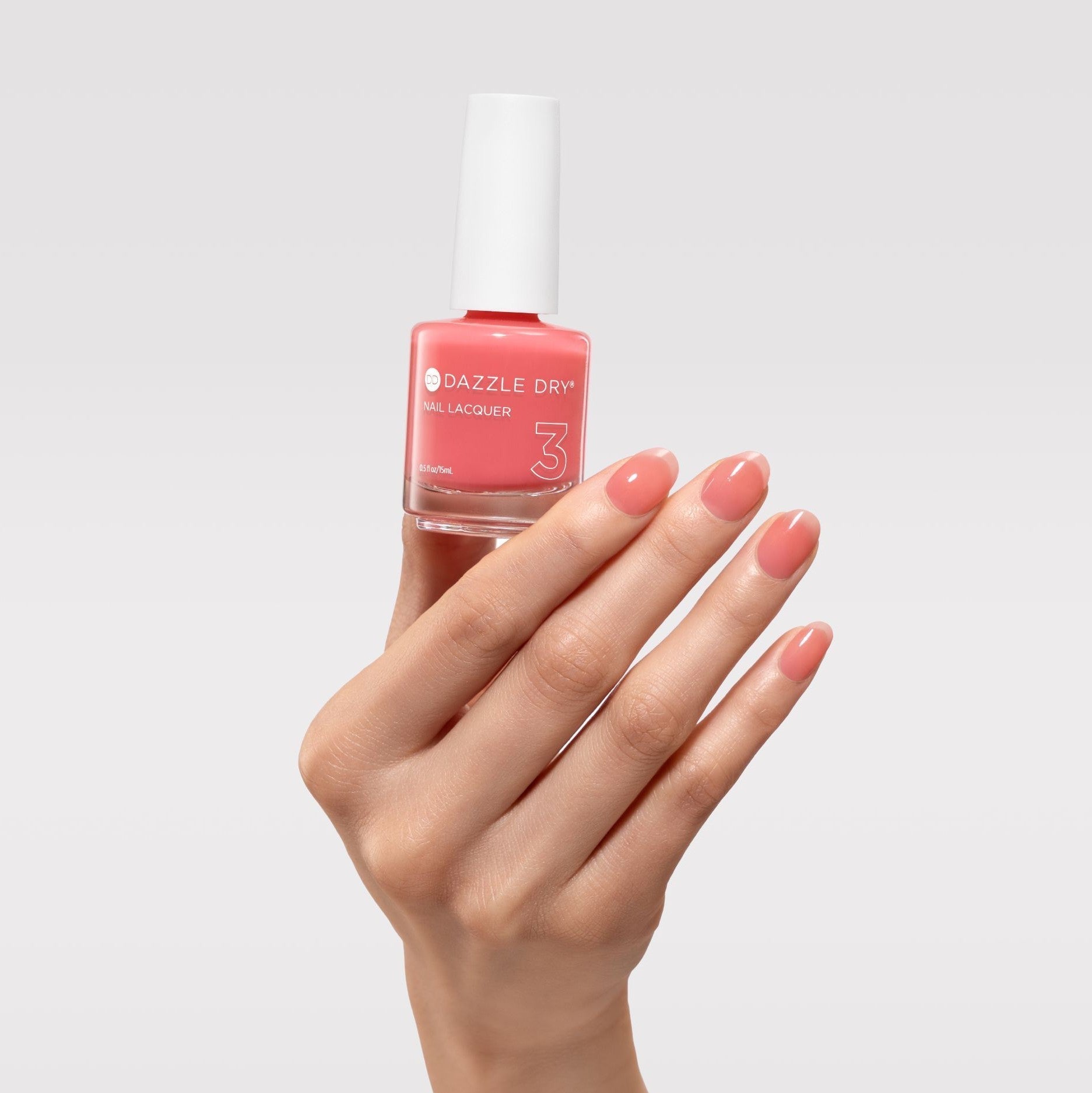 Hand holding a bottle of Dazzle Dry nail polish with matching pink nails on a light gray background