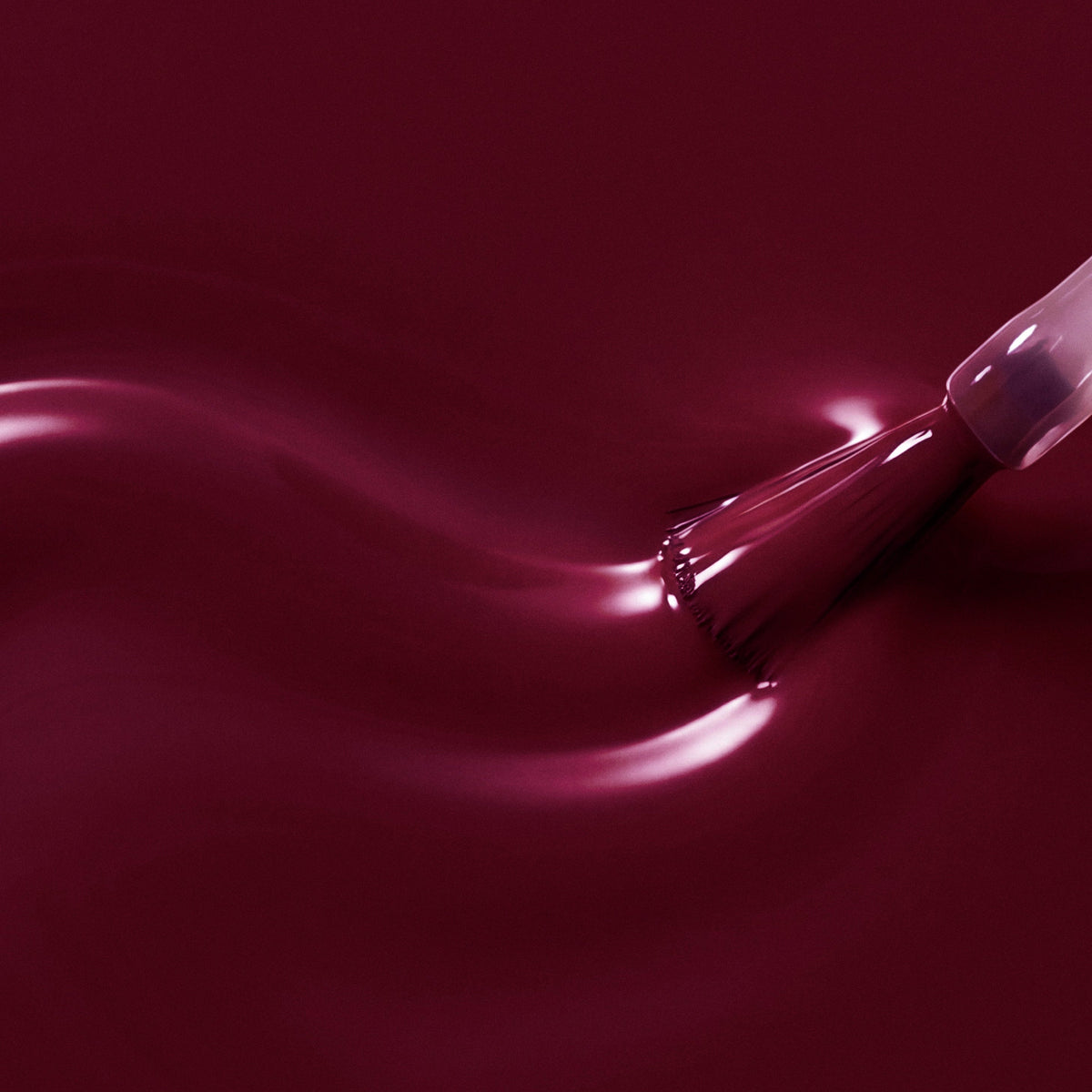 A close-up of a glossy deep burgundy liquid with a brush applying or spreading it across the surface, creating smooth waves and reflective highlights.