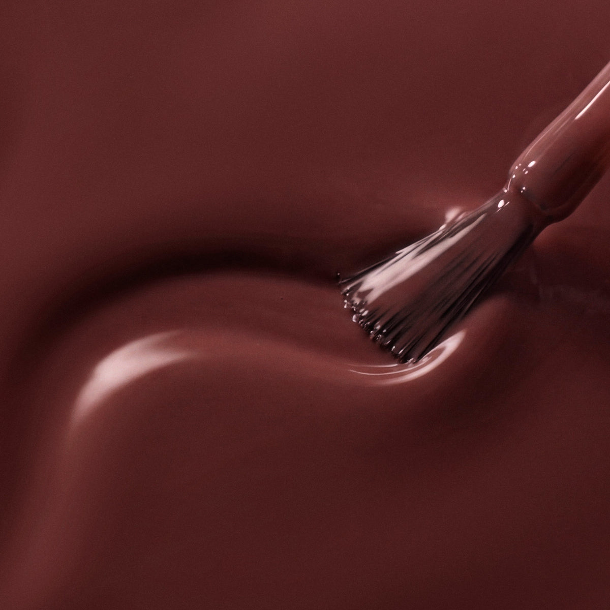 A close-up of glossy dark brown nail polish with a brush applying or smoothing the finish on a smooth surface.