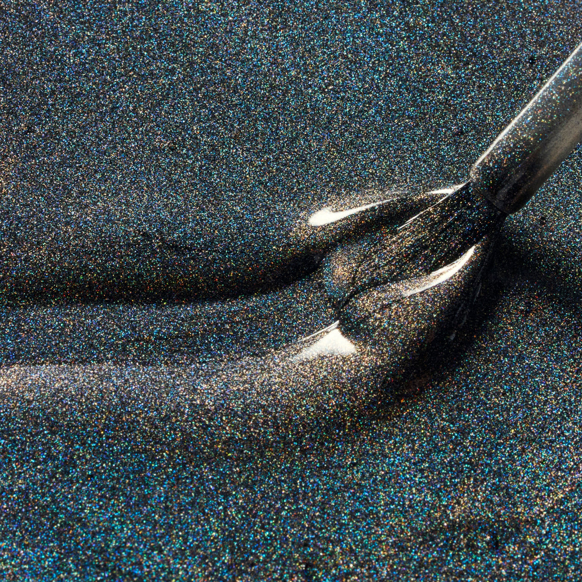 Close-up of a dark glitter nail polish brush applying shimmering black nail polish with fine iridescent flecks.