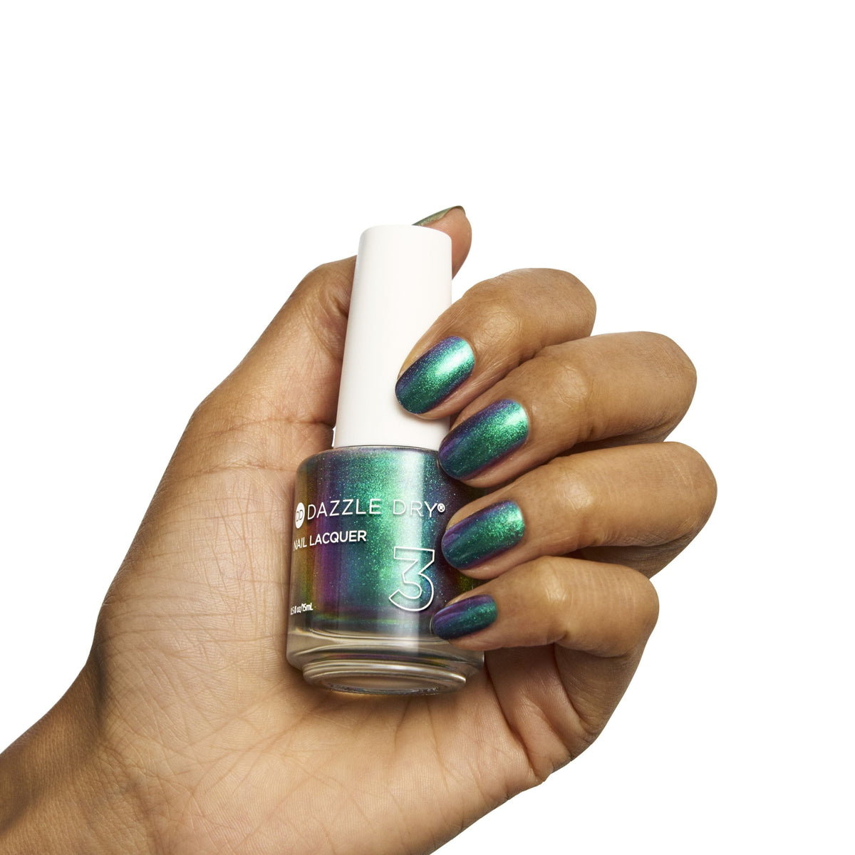 A hand holding a bottle of Dazzle Shine nail lacquer with a white cap, showcasing iridescent green and purple nail polish on fingernails against a solid white background.