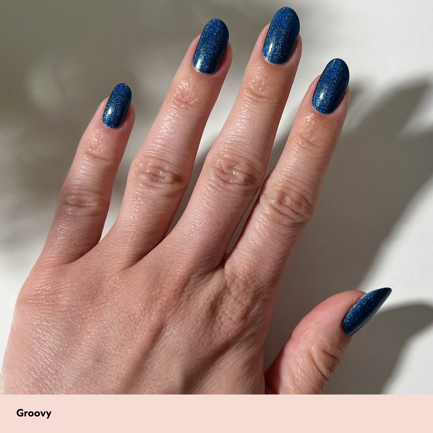 Hand with blue glittery nail polish on a neutral background