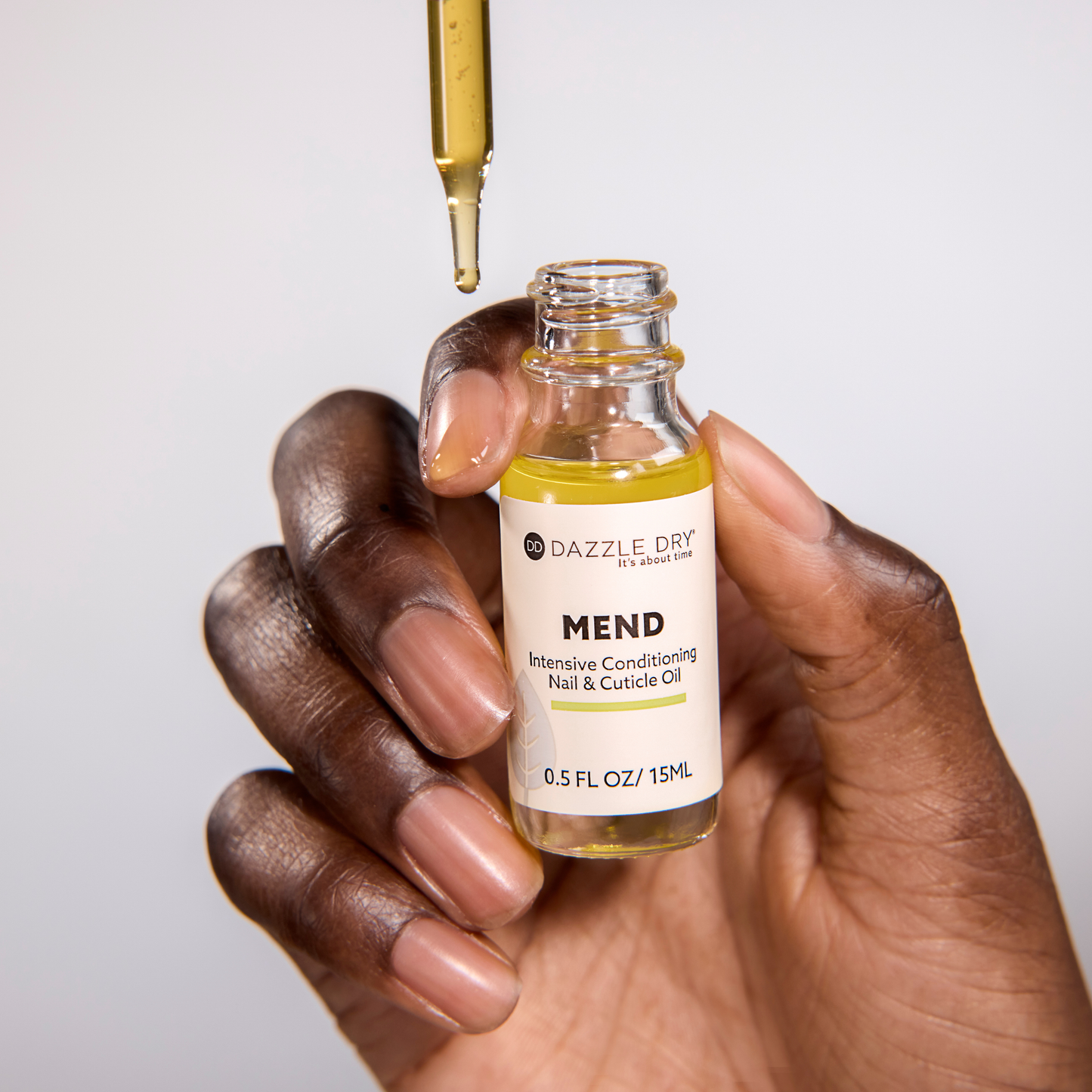 Hand holding a bottle of Dazzle Dry Mend Intensive Conditioning Nail & Cuticle Oil with a dropper.