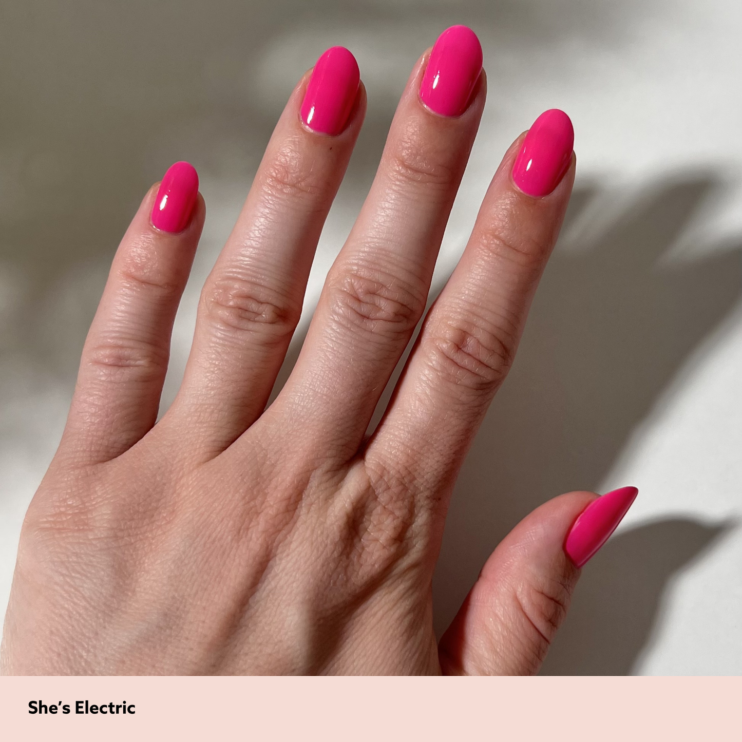 Hand with bright pink nails on a neutral background