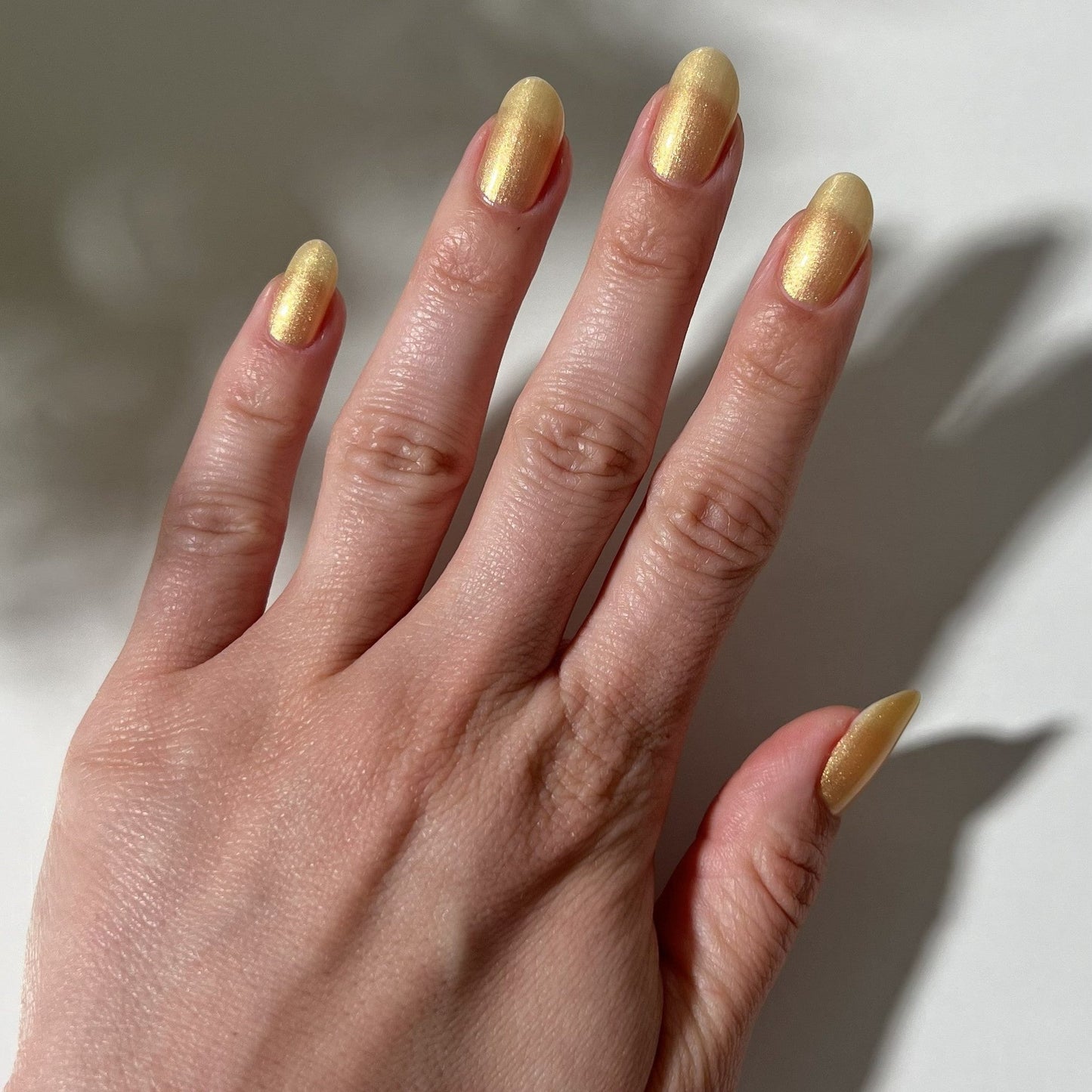Hand with gold nail polish on a neutral background