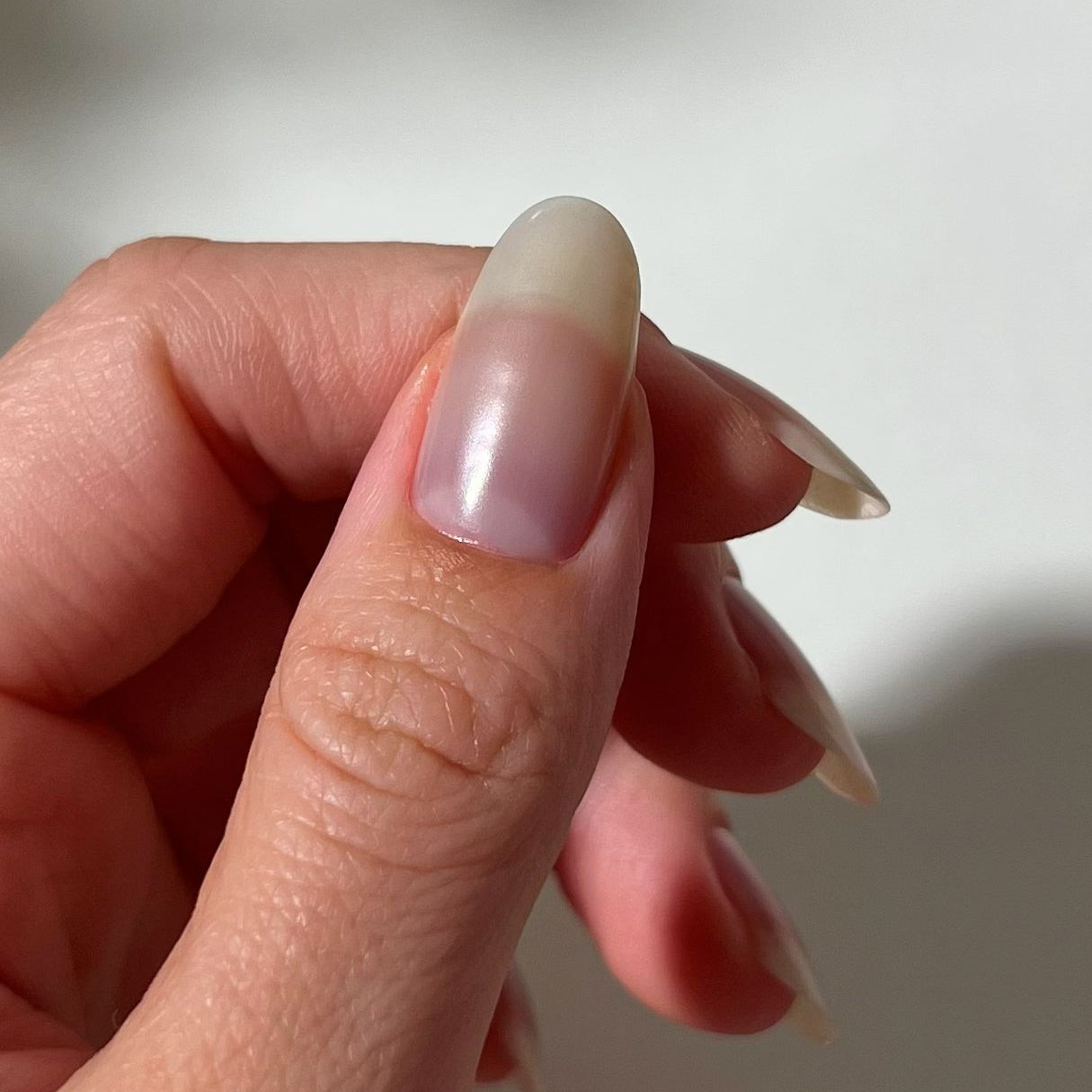 Close-up of a hand with a gradient nail color against a neutral background